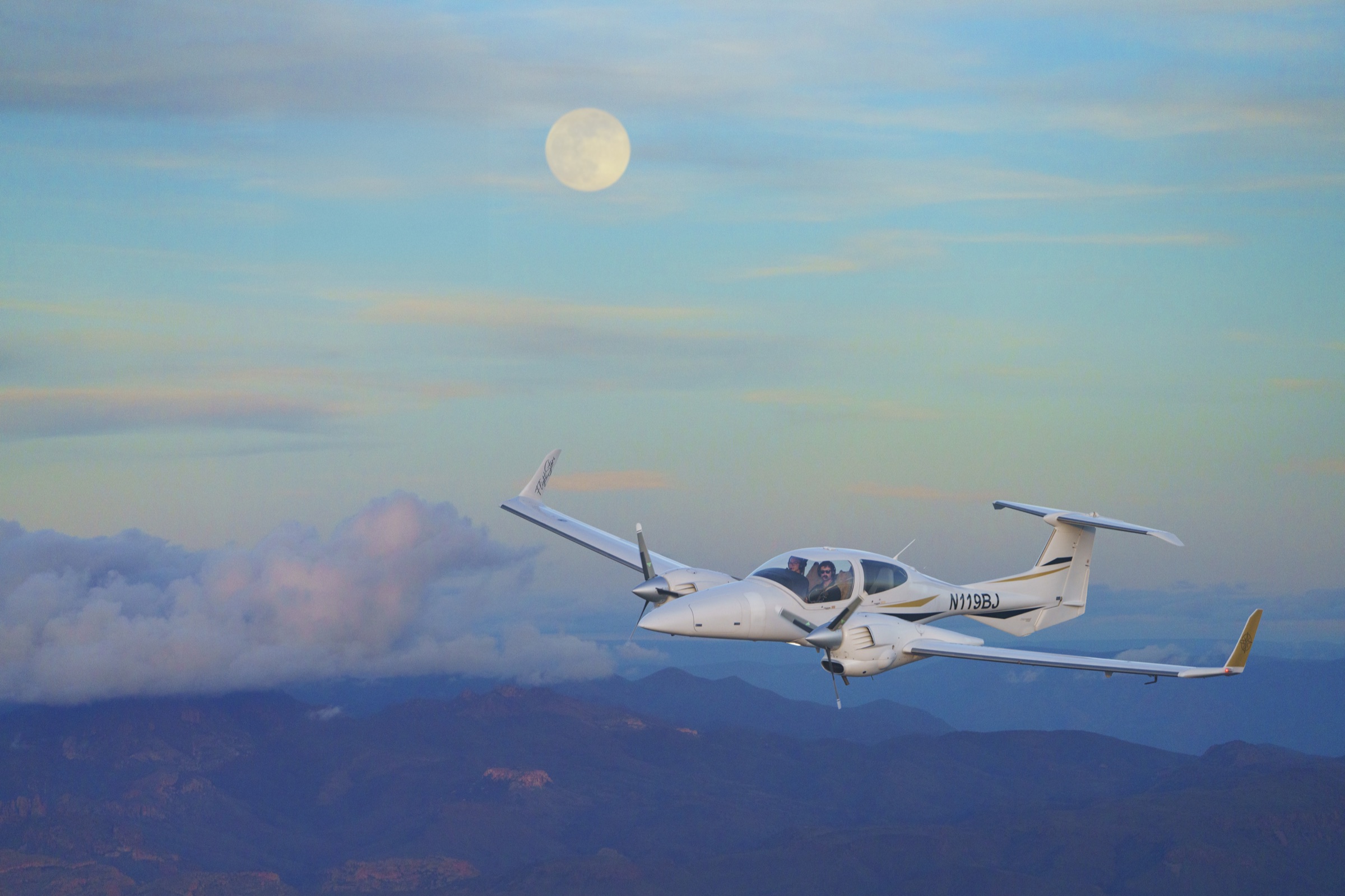 The Flight Stars Diamond DA42 air-to-air at dusk with the moon rising over the red-rock range